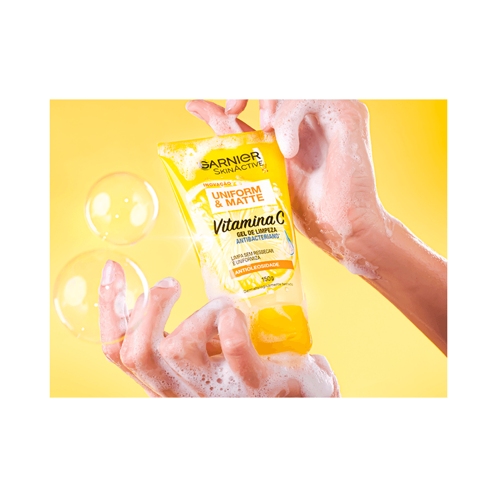 Mãos ensaboadas segurando o tubo do Gel Garnier com bolhas, transmitindo sensação de limpeza
