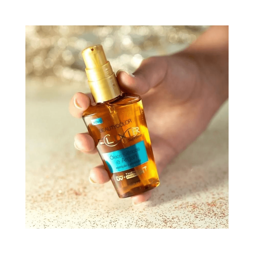 Mão segurando o frasco âmbar do Elixir Capilar Beauty Color, destacando brilho do óleo