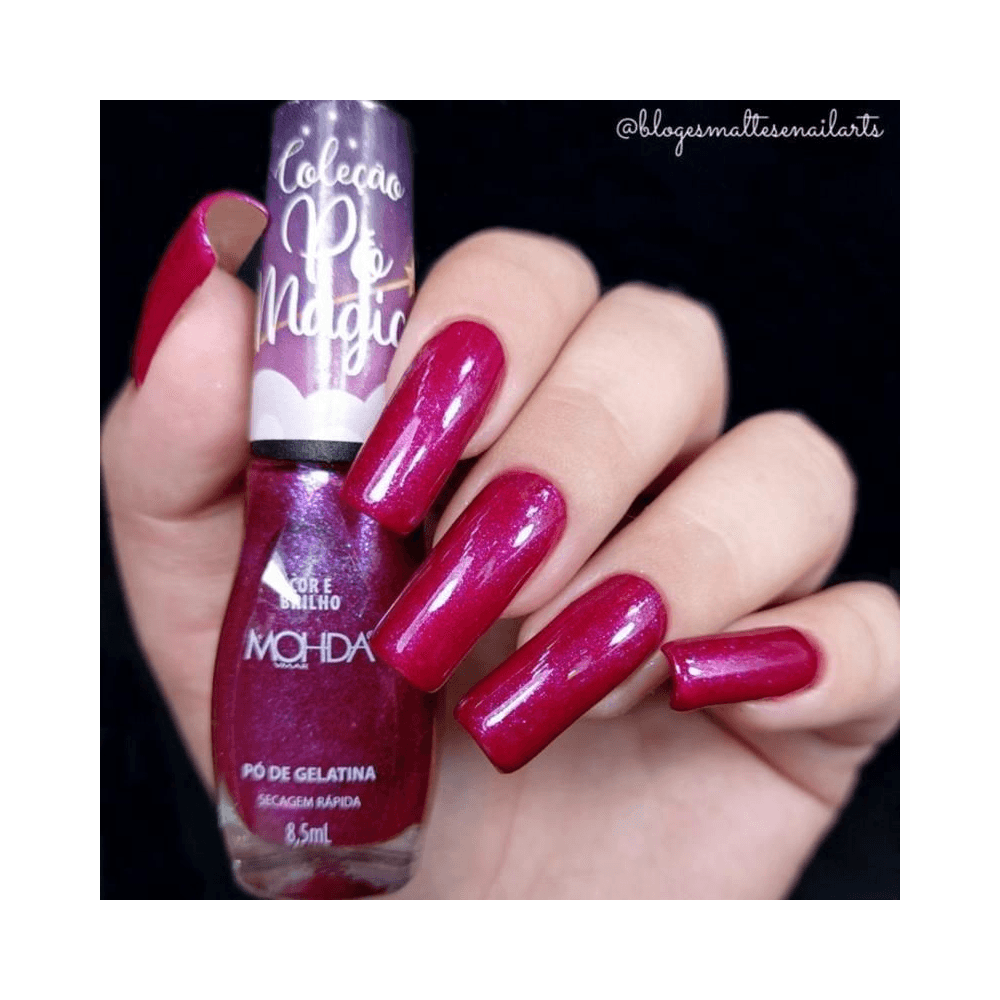 Mão com unhas esmaltadas na tonalidade roxa perolada segurando o frasco Mohda