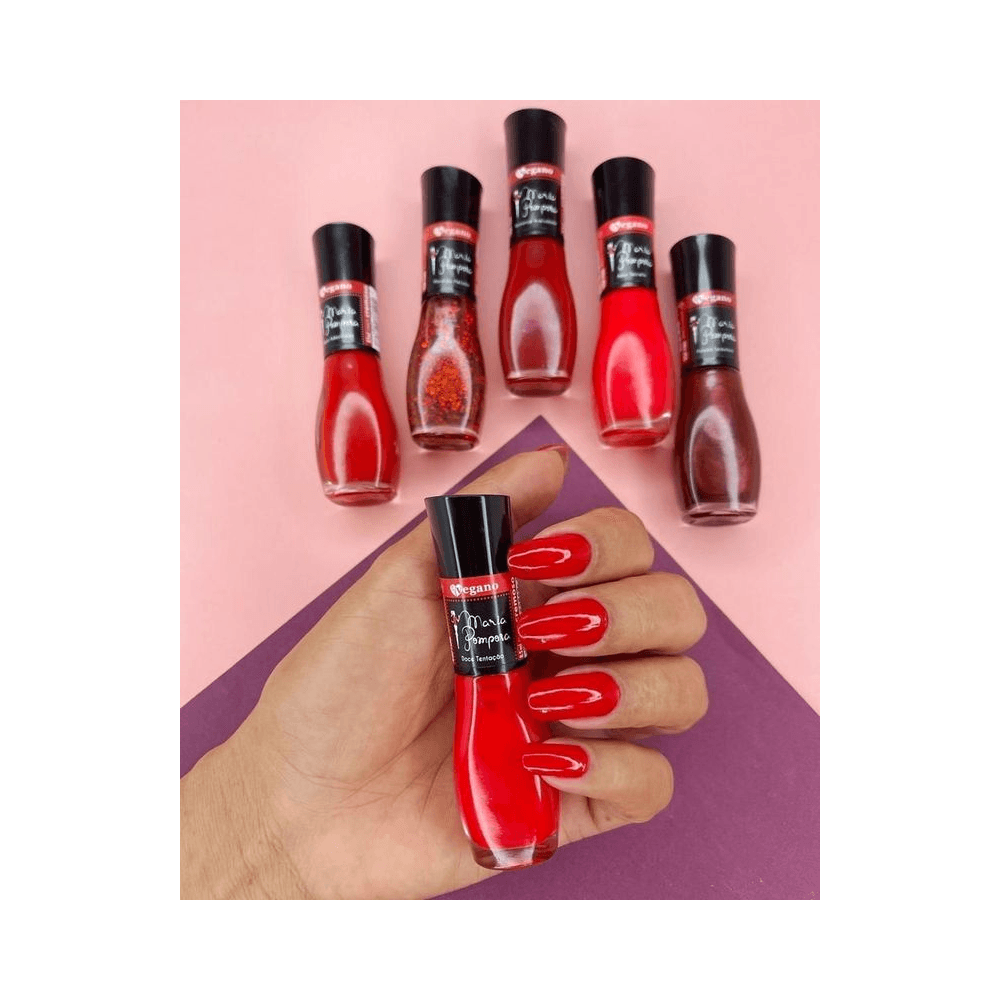 Mão com unhas esmaltadas em vermelho vibrante segurando frasco Maria Pomposa