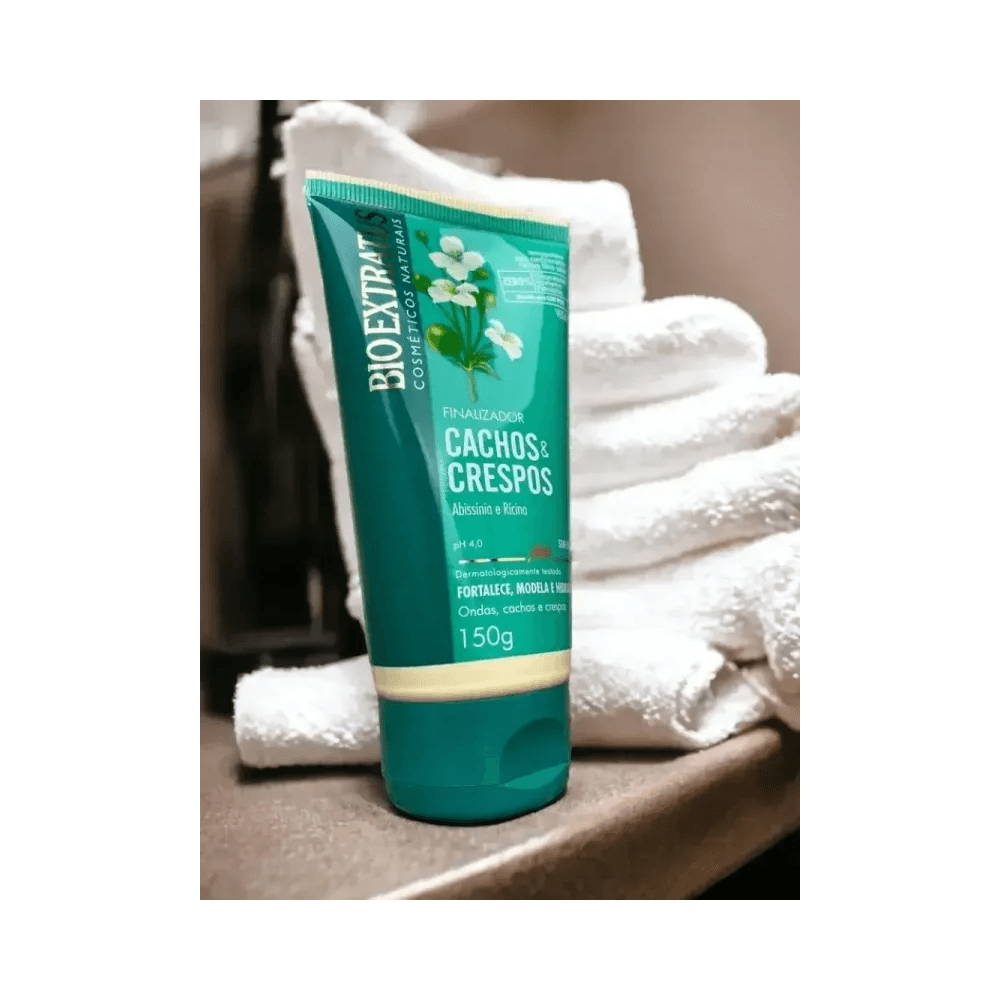 Tubo do finalizador Bio Extratus Cachos & Crespos 150g sobre superfície marrom com toalhas ao fundo